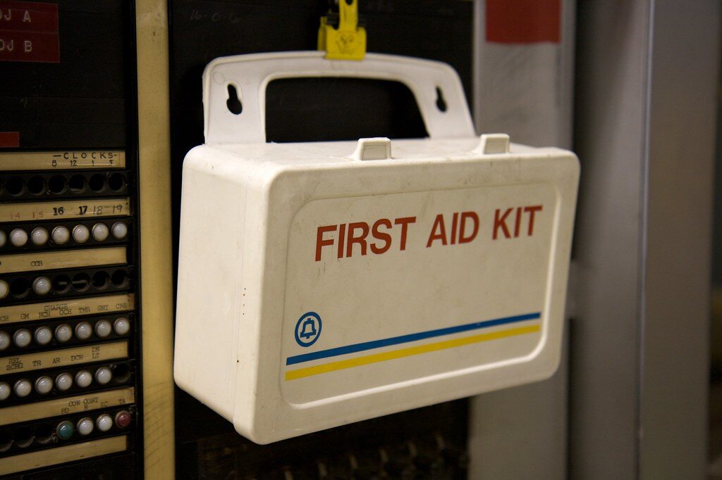 Weißer Erste-Hilfe-Kasten mit der Aufschrift First Aid Kit hängt an einem alten Schaltschrank