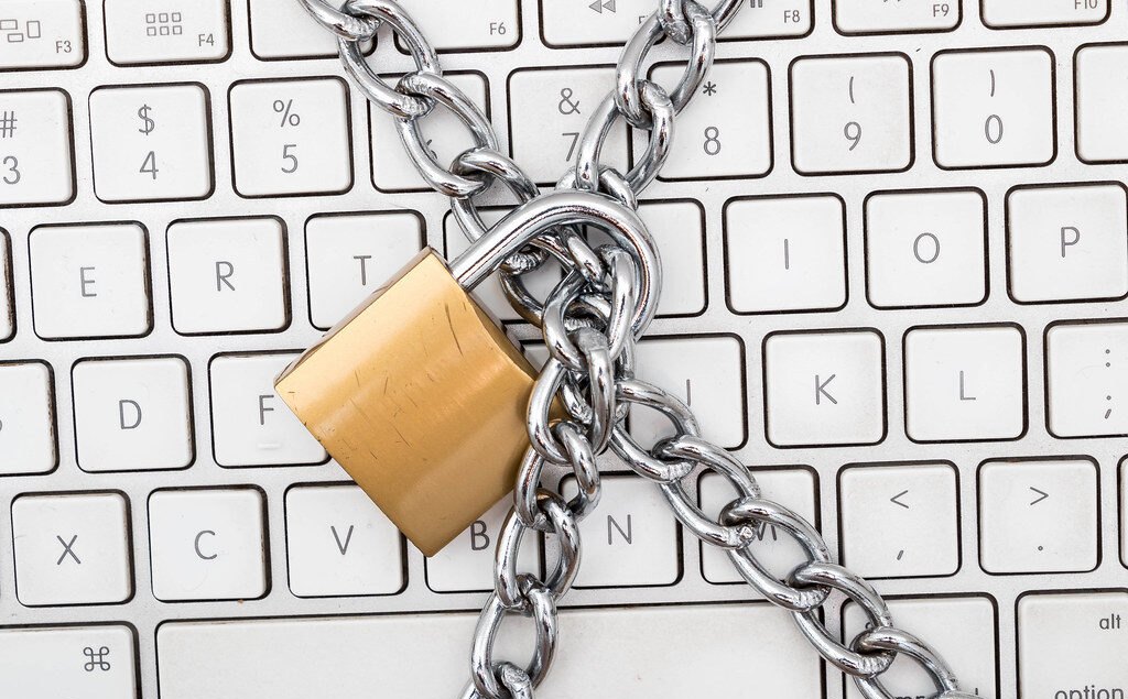 Ein Vorhängeschloss mit einer Metallkette liegt auf einer weißen Computertastatur